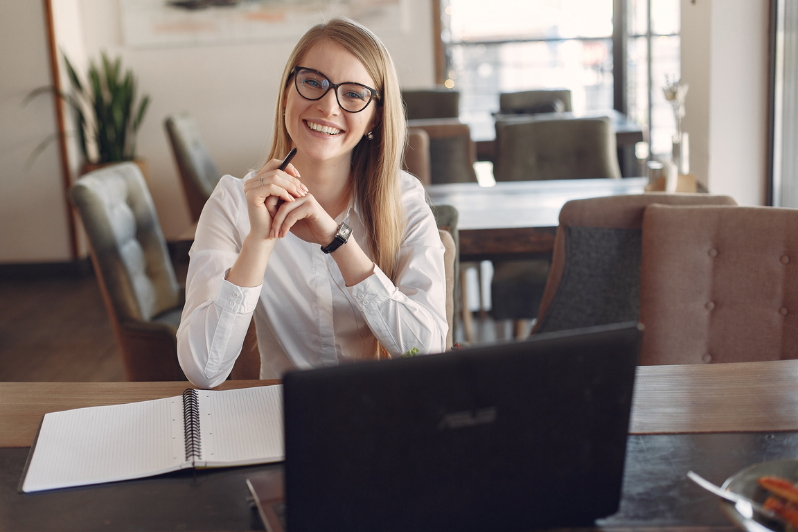 Cheerful young businesswoman in eyeglasses during remote work in cafeteria